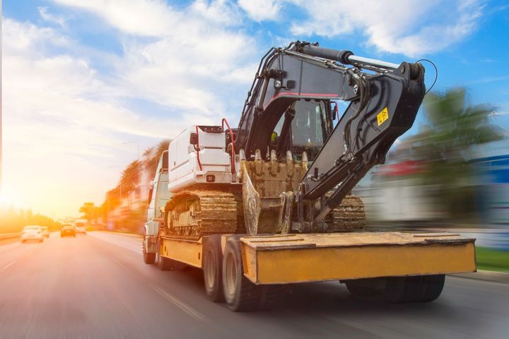 Une lourde excavatrice chargée sur un camion plateau circulant sur une route au coucher du soleil