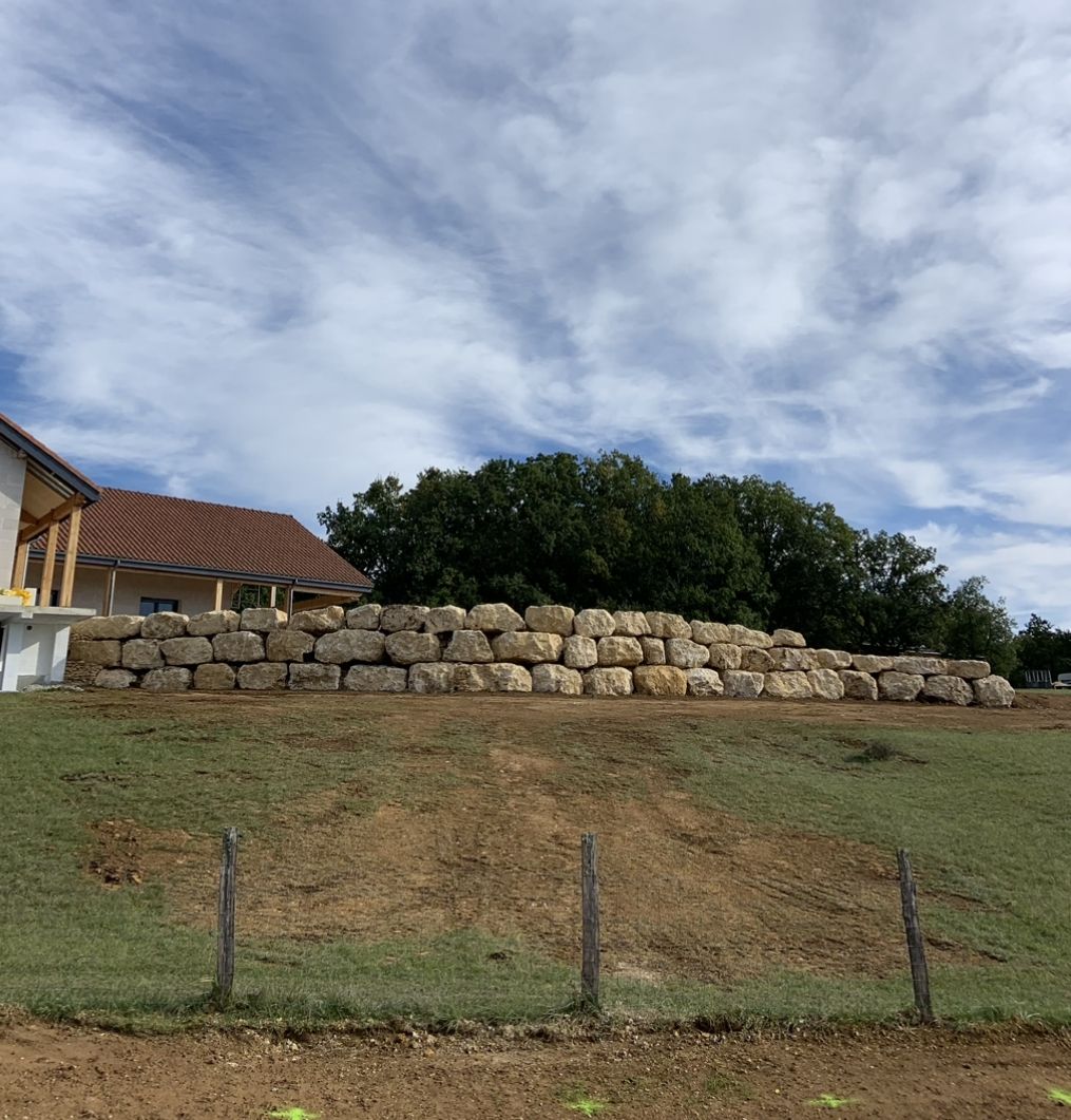 Colline herbeuse avec des bottes de foin empilées à côté d'une maison sous un ciel nuageux