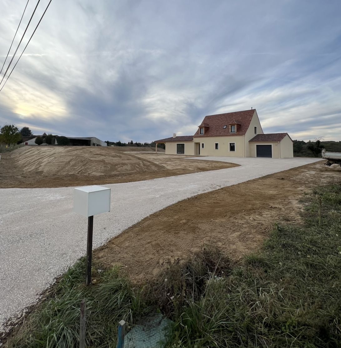 Maison de campagne avec une allée de gravier sous un ciel nuageux, avec une boîte aux lettres au premier plan.