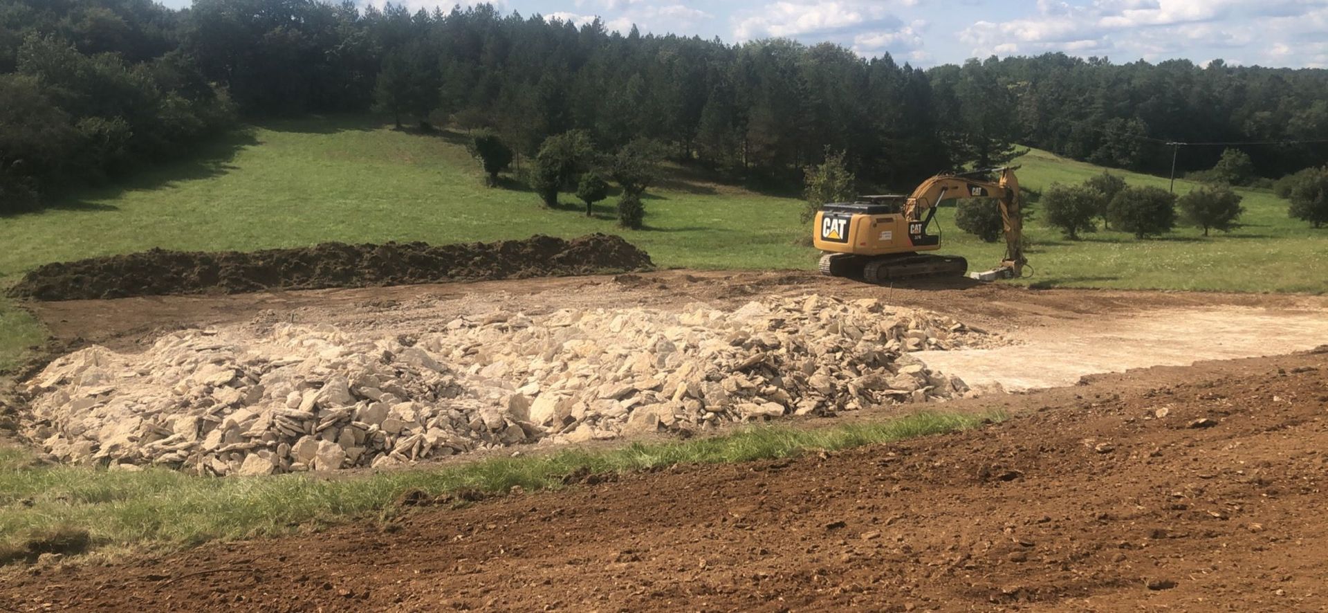 Un bulldozer nivelle le terrain sur un chantier de construction rural avec des arbres et des champs en arrière-plan.