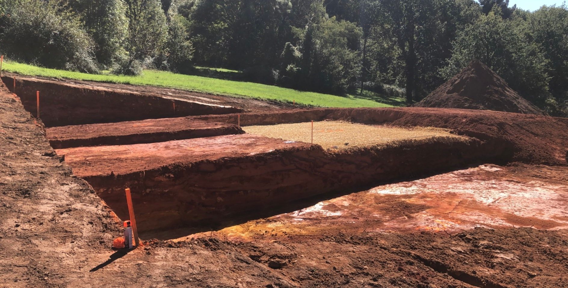 Terrasses de terre excavées à flanc de colline, avec de la terre rouge, de l'herbe verte et des arbres en arrière-plan.