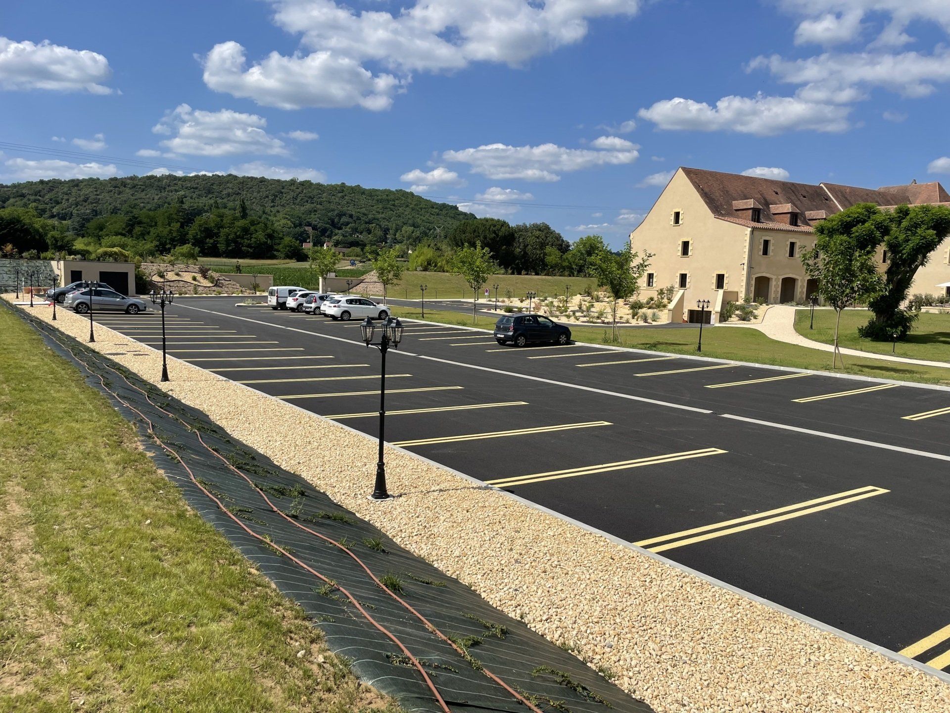 Parking vide à côté d'un bâtiment beige sous un ciel bleu parsemé de nuages.