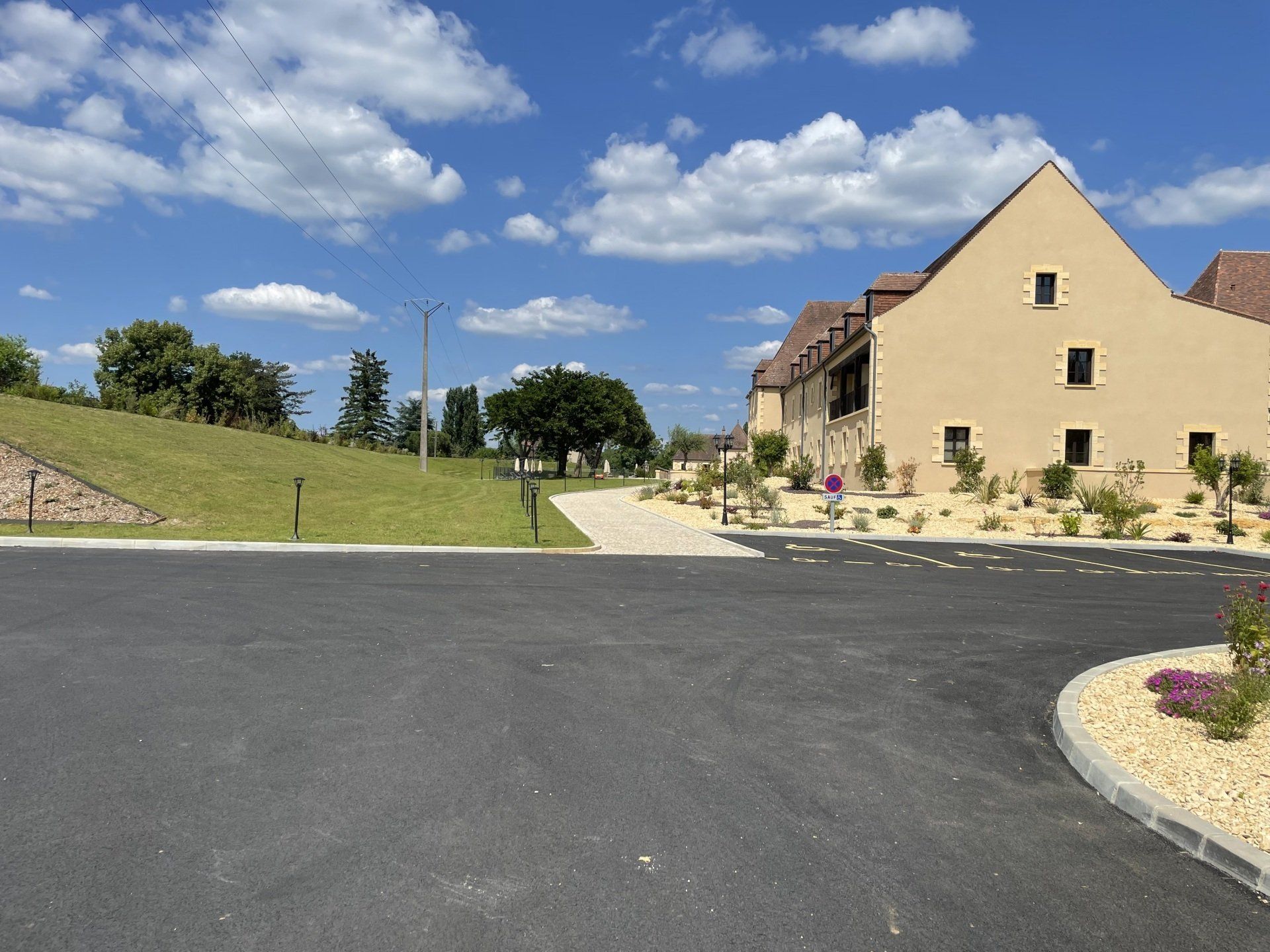 Vue depuis la rue de bâtiments beiges, de pelouses aménagées et d'asphalte désert sous un ciel bleu parsemé de nuages.