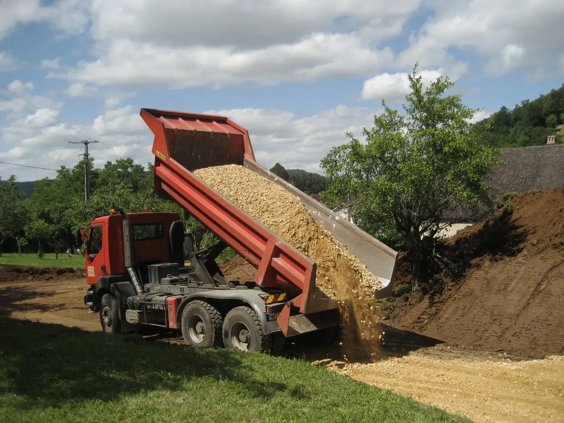 Un camion-benne décharge du gravier sur un tas de terre sur un chantier de construction.