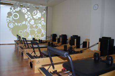 Una fila de máquinas de pilates en un gimnasio con un reloj en la pared.