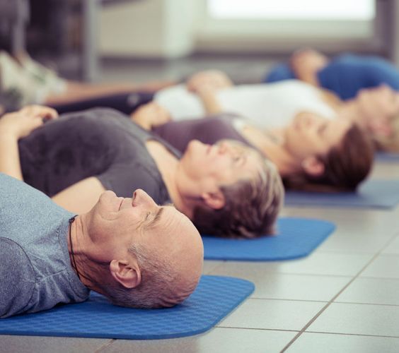Un grupo de personas están tumbadas sobre colchonetas de yoga con los ojos cerrados.