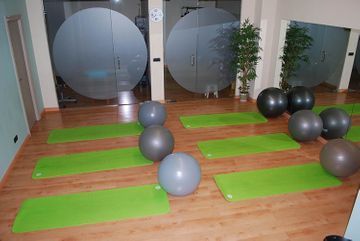 Una habitación llena de colchonetas de yoga verdes y pelotas de ejercicio.