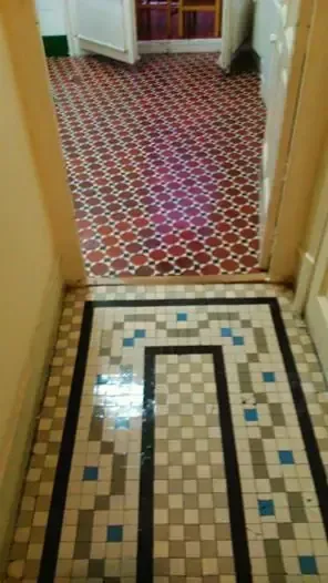Pasillo de azulejos con patrón geométrico que conduce a una habitación con piso con estampado rojo y blanco.