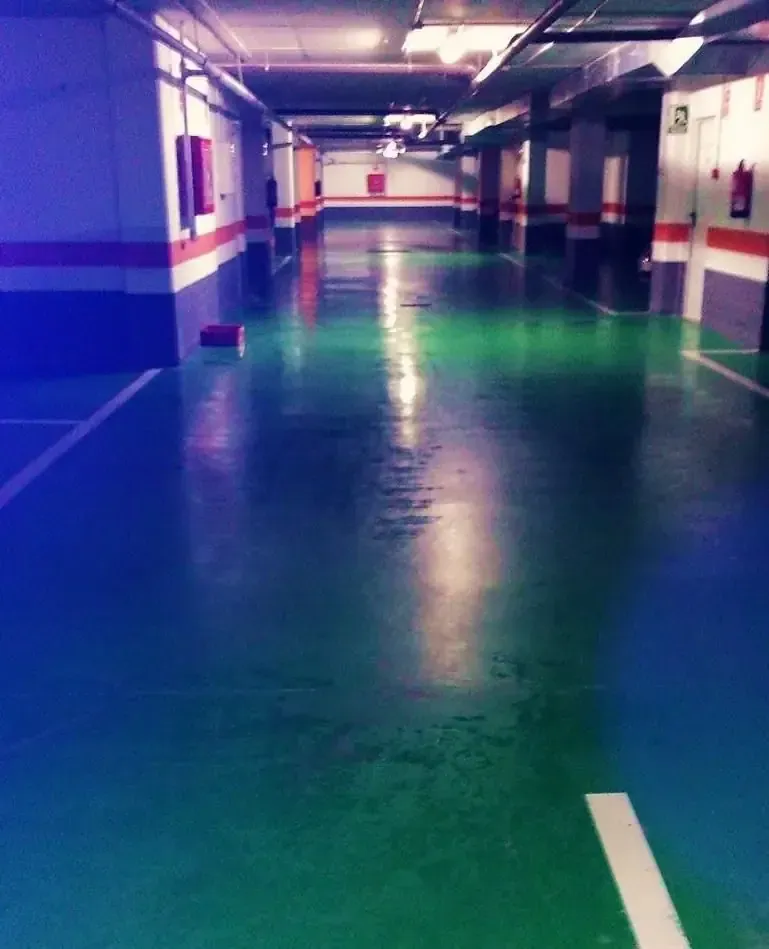 Un estacionamiento vacío con piso pintado de verde y azul, líneas blancas y equipo contra incendios de color rojo.