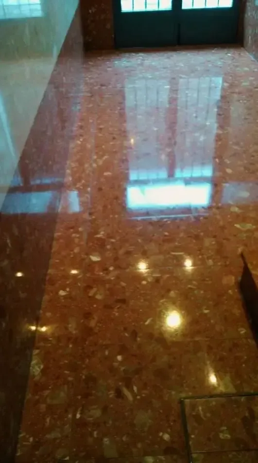 Suelo de terrazo rojo brillante con reflejos de puerta y ventanas.