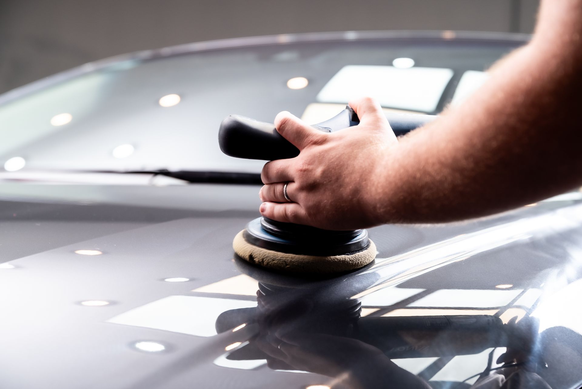 Gros plan sur une personne utilisant une polisseuse double action pour polir le capot d'une voiture grise.
