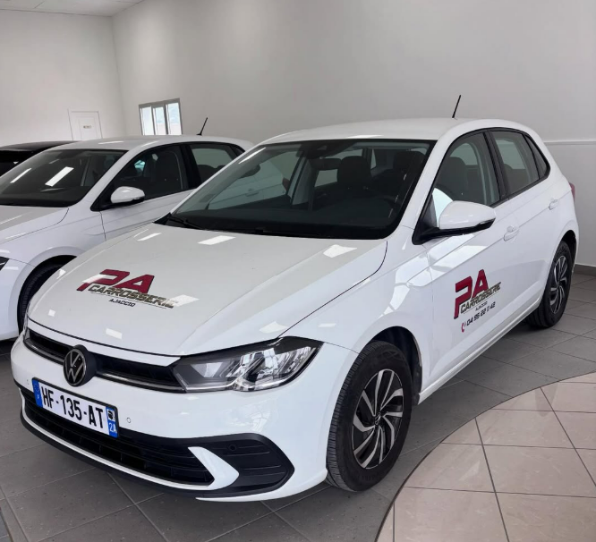 Une Volkswagen Polo blanche garée à l'intérieur, arborant le logo rouge de la marque sur le capot et la portière côté conducteur.