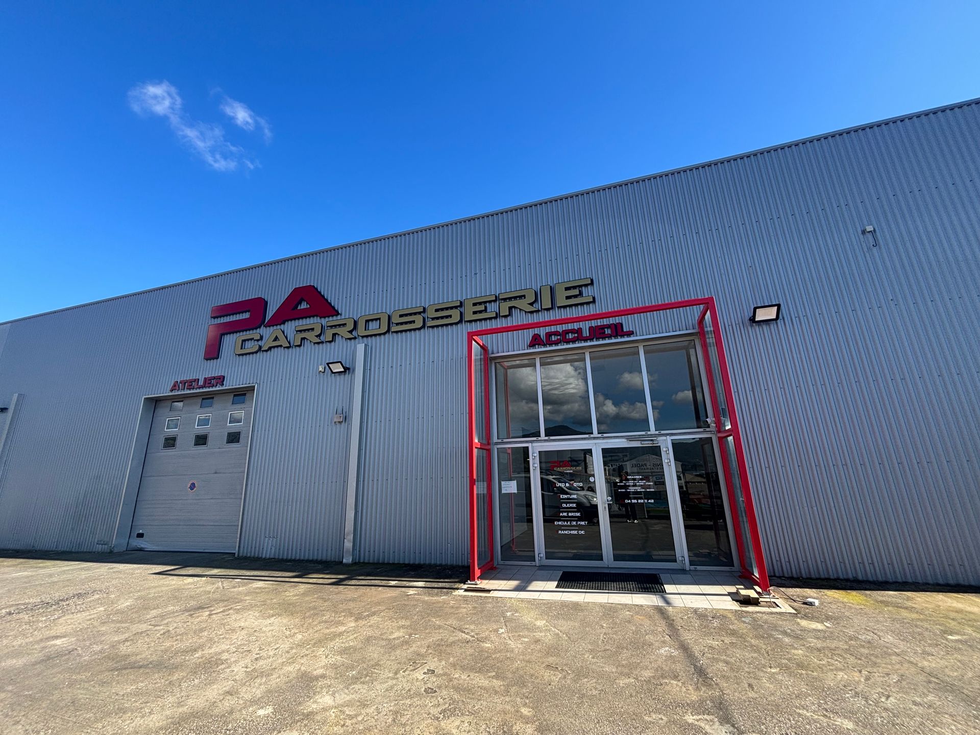 Extérieur d'un atelier de carrosserie automobile, avec une entrée encadrée de rouge.