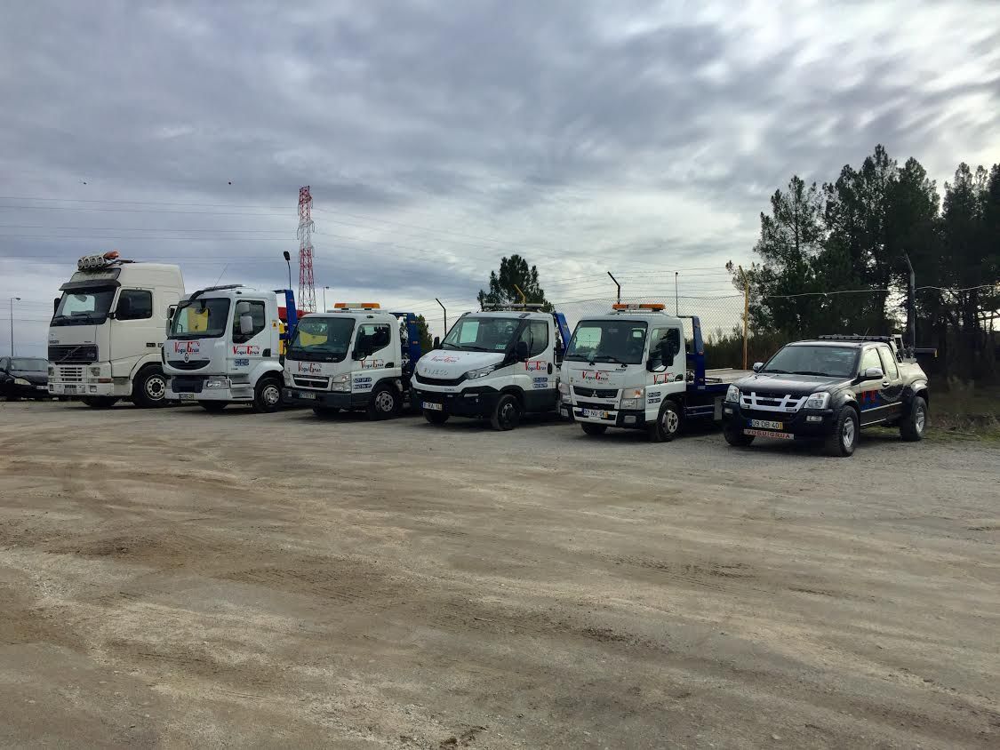 Caminhões-guincho estacionados em um terreno de cascalho sob um céu nublado.