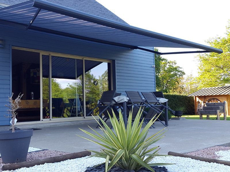 Maison à bardage bleu avec un store banne sur une terrasse
