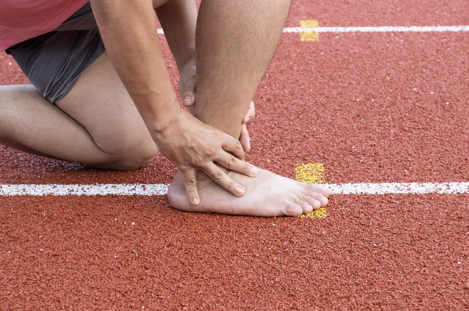 Persona en una pista de carreras sujetándose el tobillo, posiblemente lesionado.