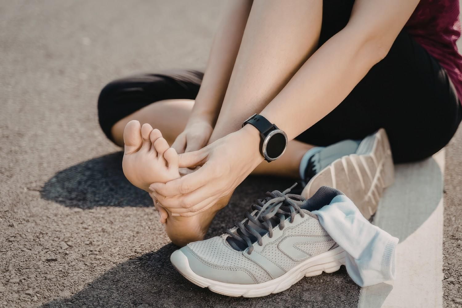 Persona sentada en el suelo, sosteniendo con dolor el pie al lado de una zapatilla para correr.