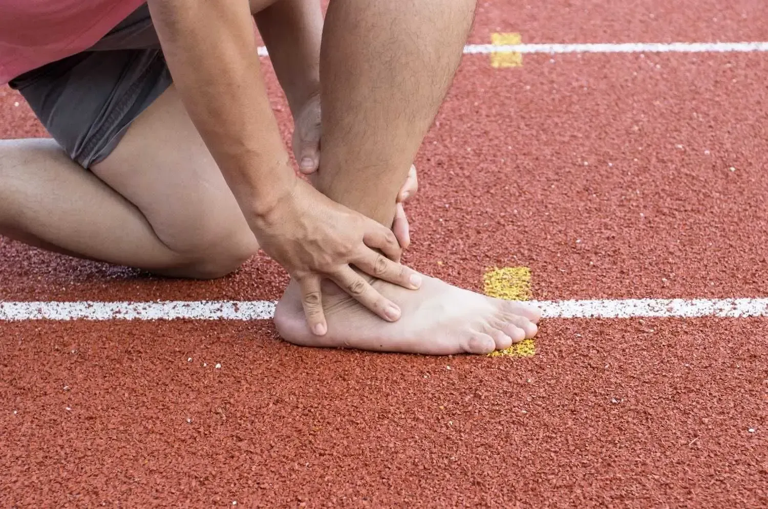 Persona en una pista de carreras sujetándose el tobillo, posiblemente lesionado.