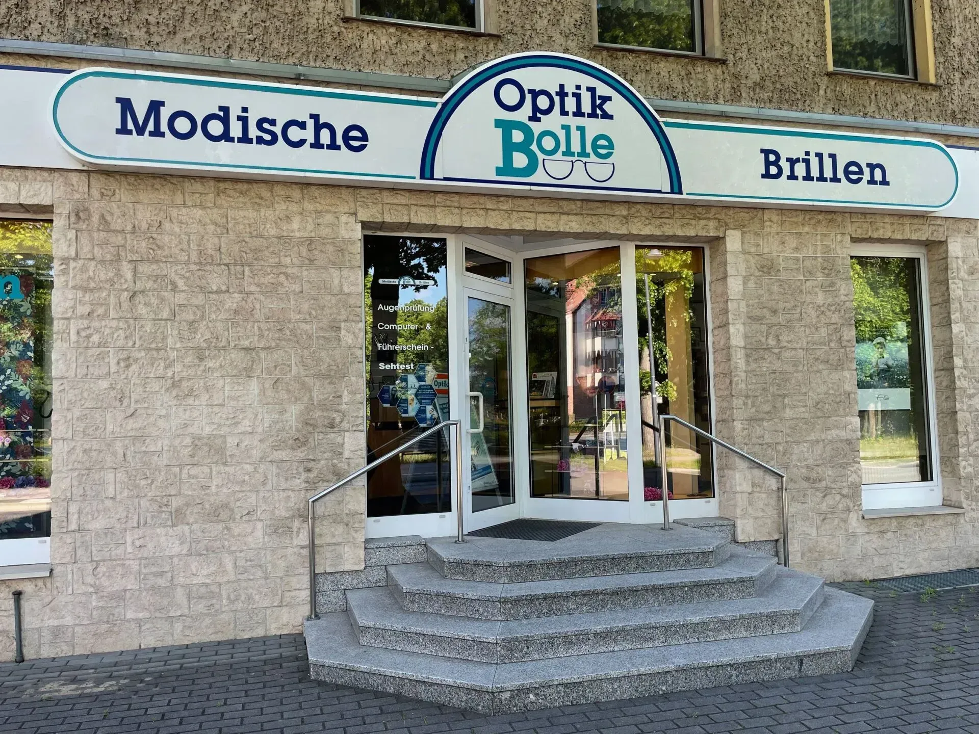Hausfassade mit Schaufenstern, Treppe und Schild am Eingang zum Optikergeschäft Optik Bolle in Wildau