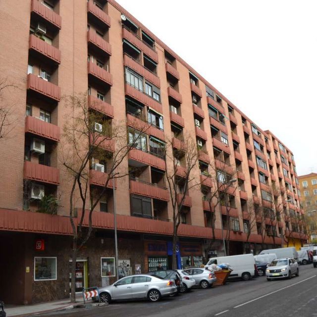 Los coches están aparcados delante de un gran edificio de apartamentos.