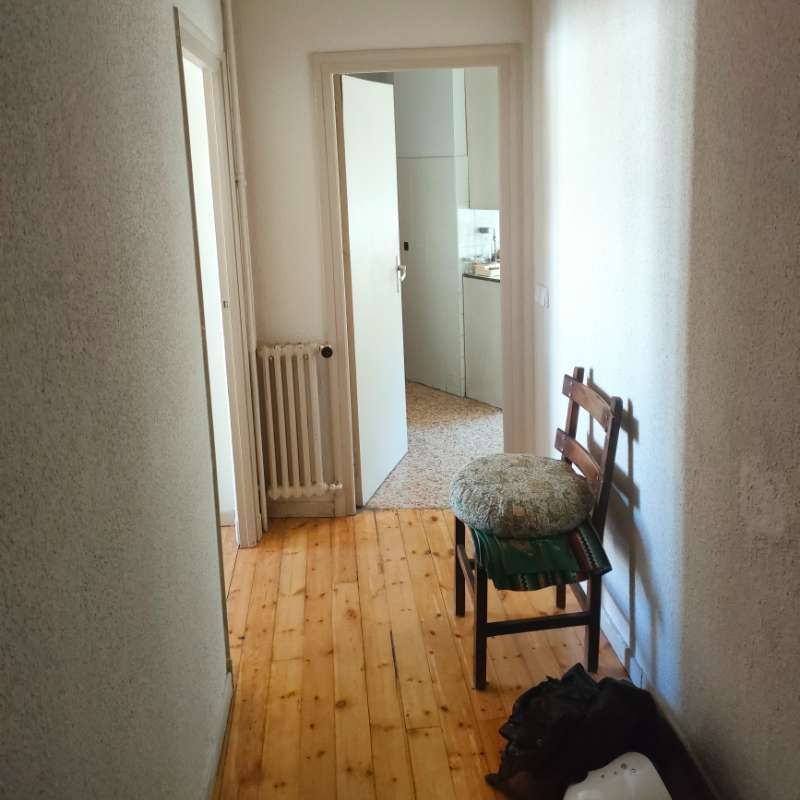 Un pasillo con suelo de madera y una silla con una almohada encima.