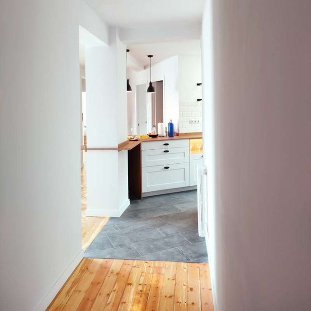 Un pasillo que conduce a una cocina con pisos de madera y gabinetes blancos.