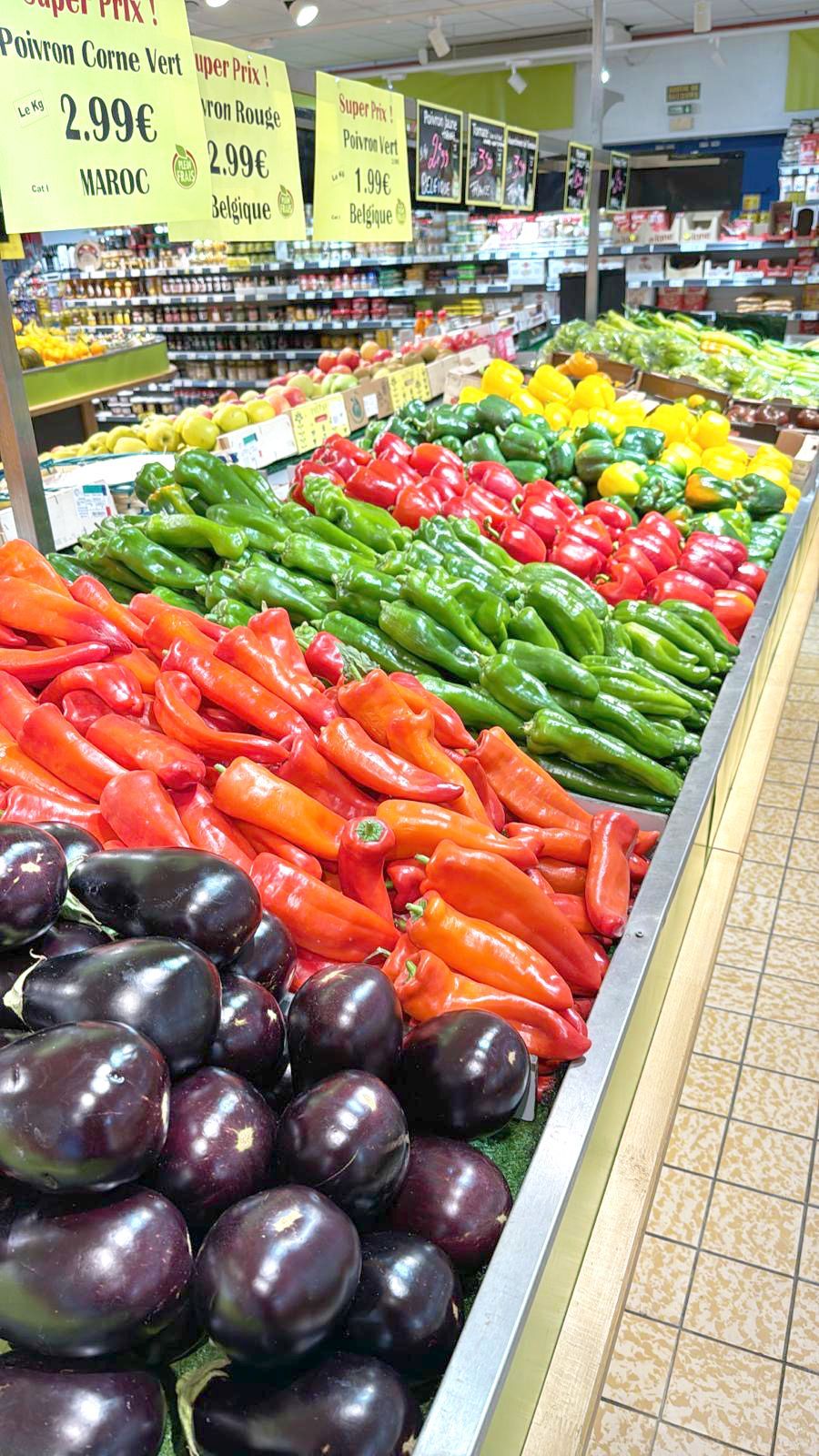 Présentation d'un rayon légumes, avec des aubergines, des poivrons rouges et verts.