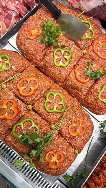 Pains de viande hachée crue décorés d'anneaux de poivron et de persil sur un plateau dans une boucherie.