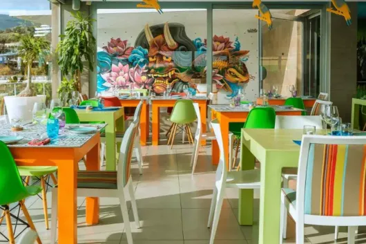 Un restaurante con mesas y sillas de colores y un mural en la pared.