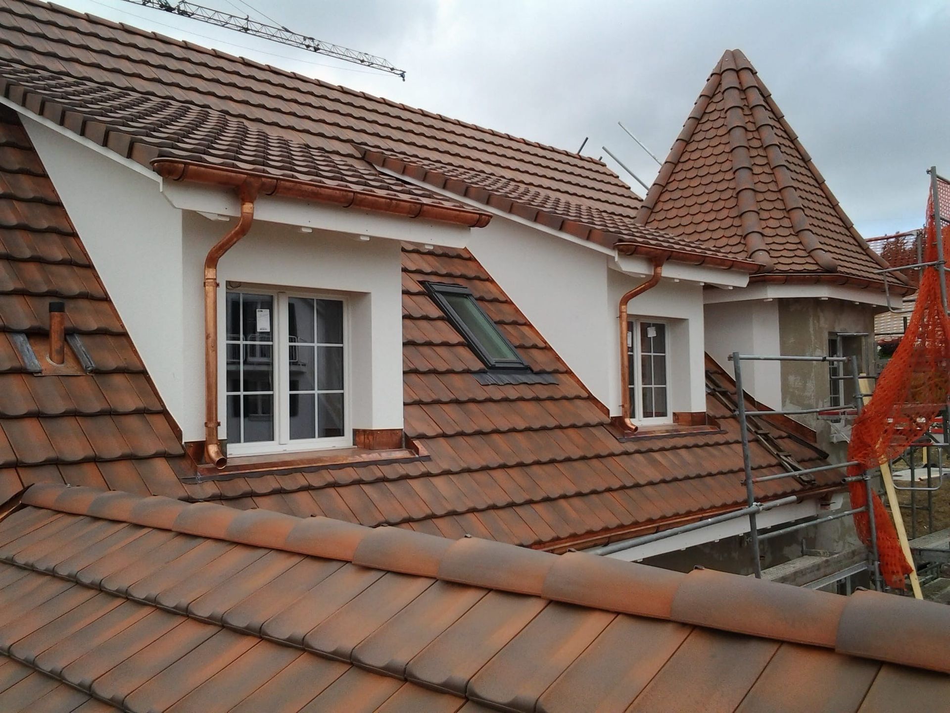 Ein Arbeiter in Arbeitskleidung verlegt rote Tondachziegel auf einem schrägen Dach.