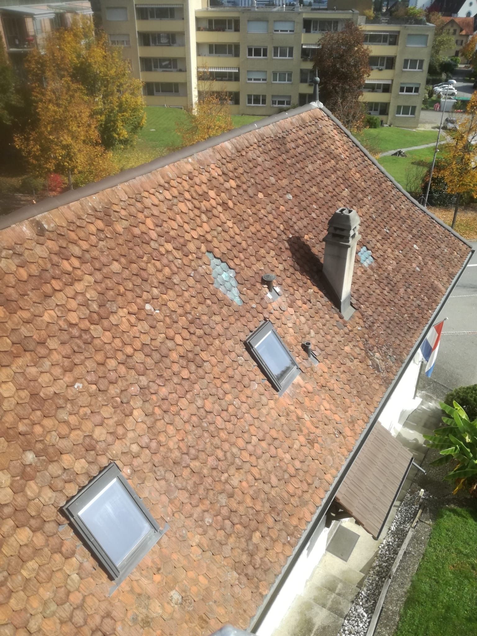 Nahaufnahme von sich überlappenden Terrakotta-Dachziegeln auf einem schrägen Dach unter klarem, blauem Himmel.