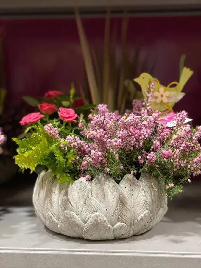 Un jarrón lleno de flores rosas y hojas verdes está sobre una mesa.