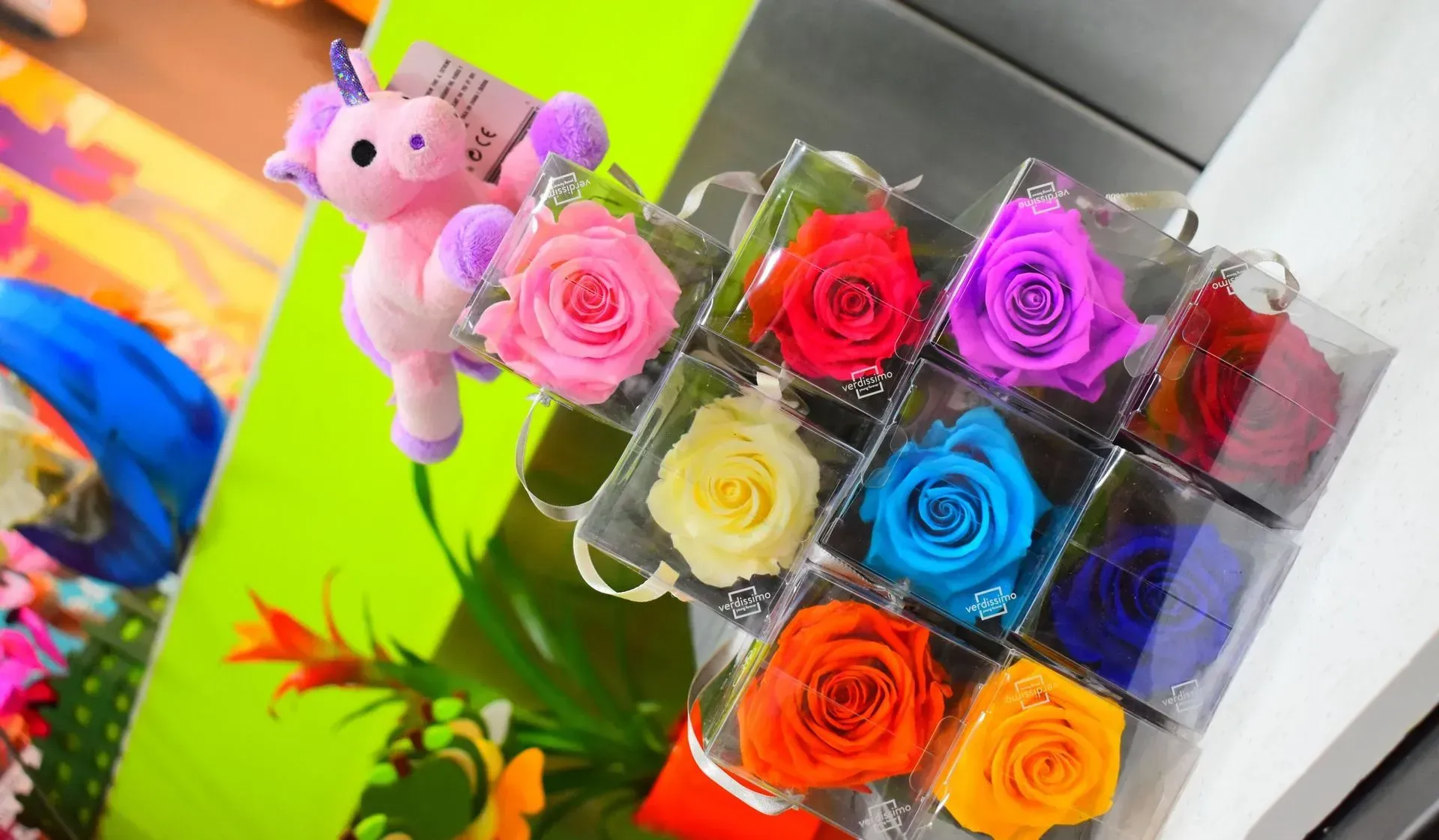 Un unicornio de peluche está sentado junto a una caja de rosas.