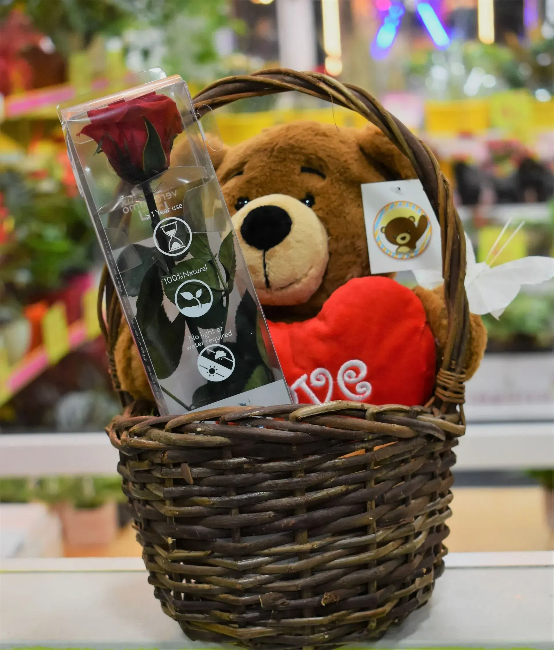 Un osito de peluche está en una canasta con un corazón rojo y una rosa.