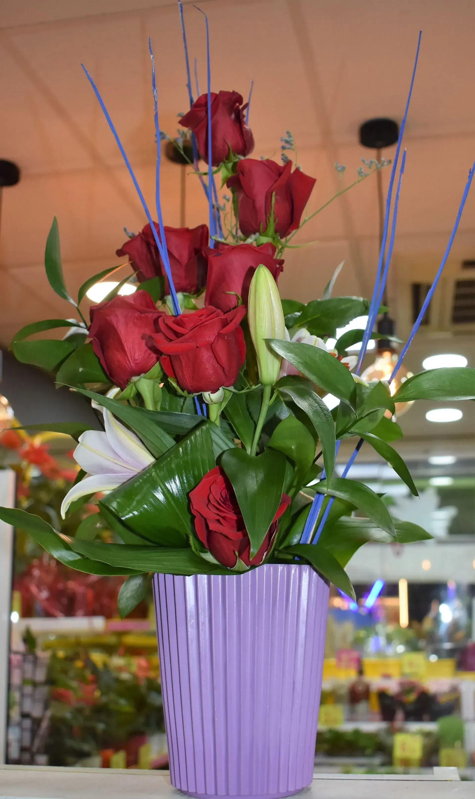 Un jarrón morado lleno de rosas rojas y lirios.