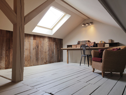 Pièce mansardée avec lambris, sol peint en blanc, puits de lumière, bureau avec chaise en métal et chaise en osier.