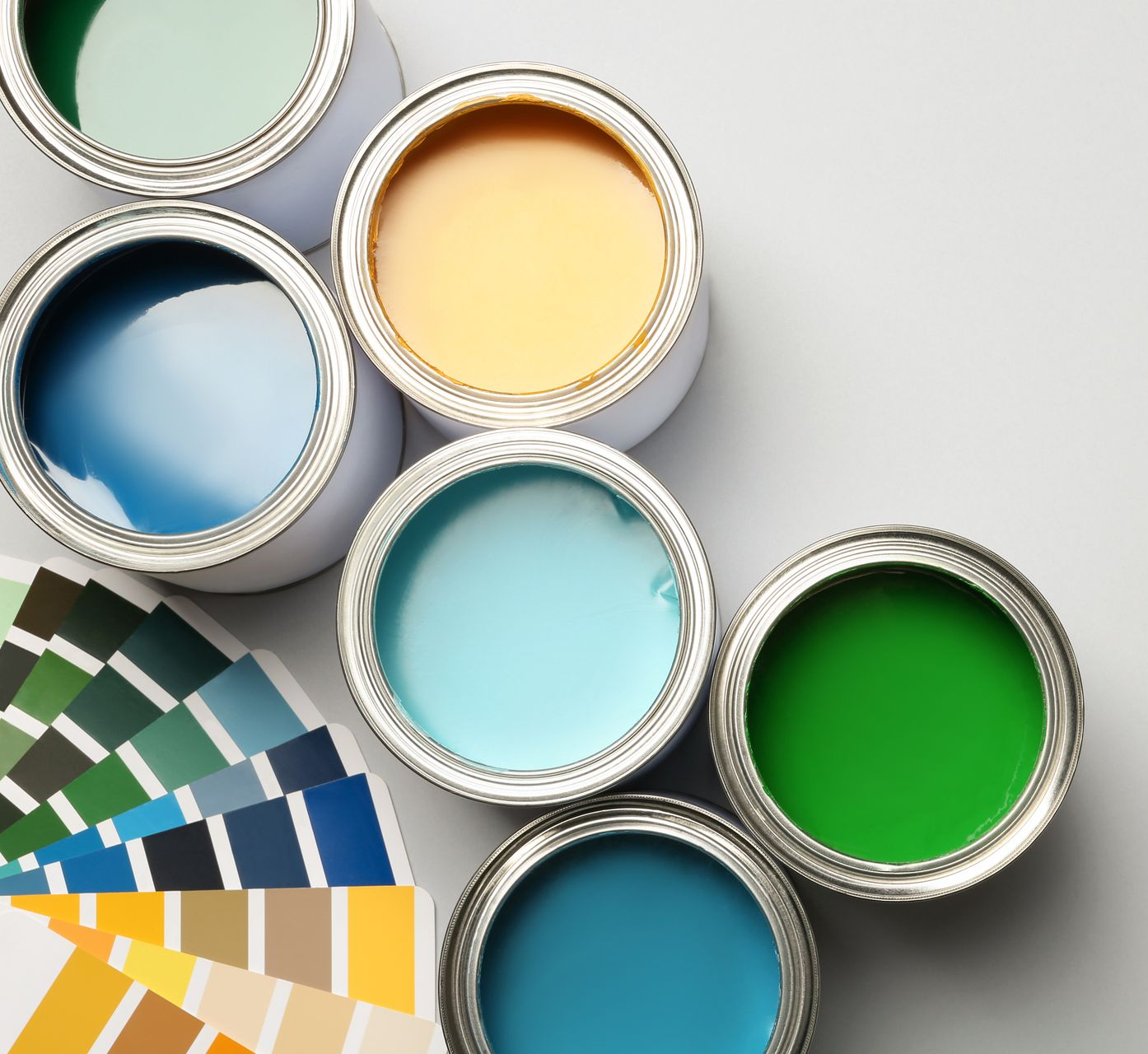 Des pots de peinture ouverts, verts, jaunes, bleus et turquoise, sont disposés à côté d'échantillons de différentes couleurs.