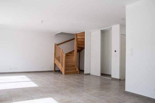 Une pièce ouverte avec des murs blancs, un sol carrelé gris et un escalier en colimaçon en bois.