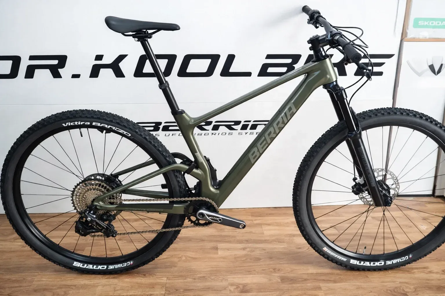 Bicicleta de montaña verde con neumáticos y componentes negros, expuesta en el interior.