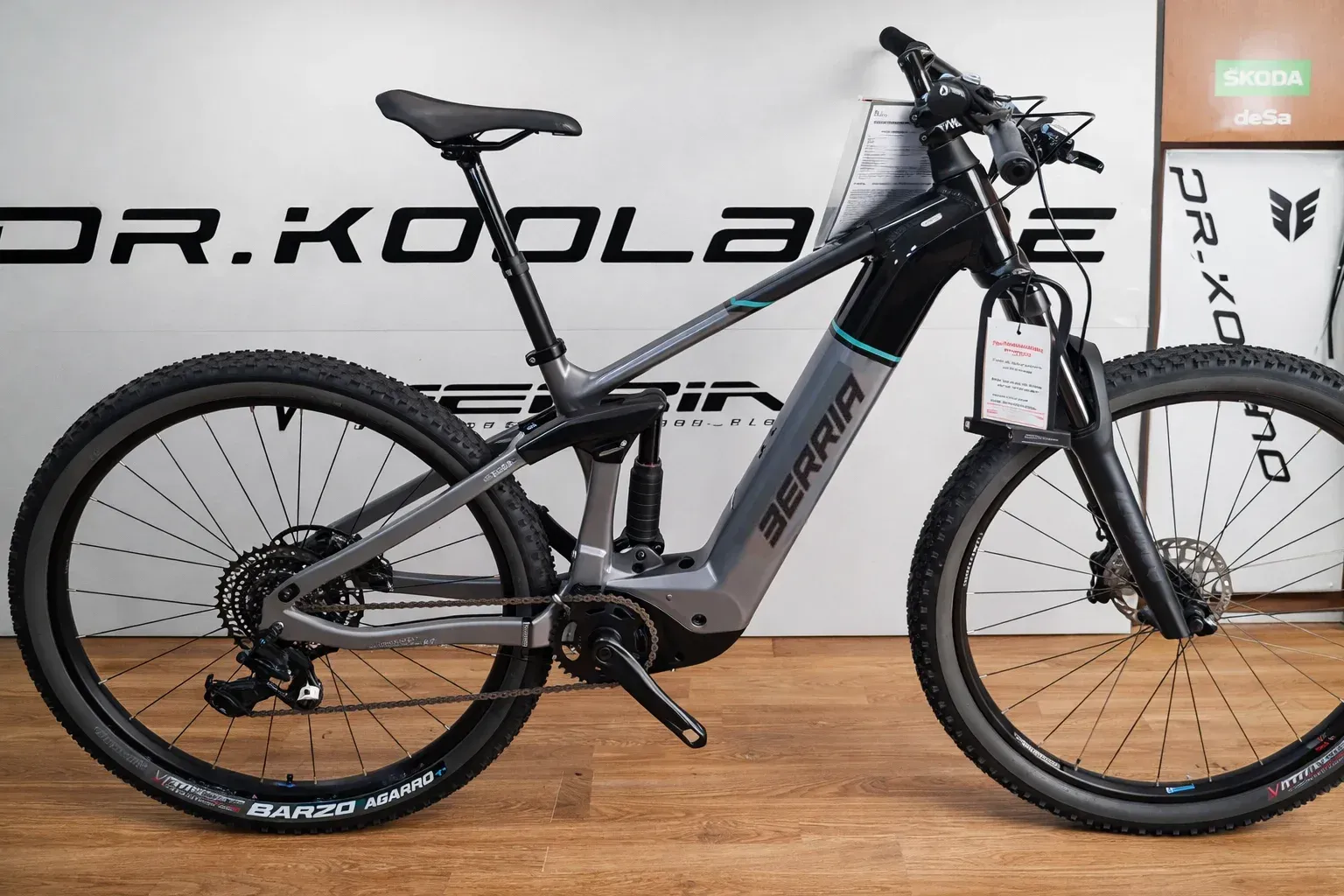 Bicicleta de montaña eléctrica, gris y negra con detalles en verde azulado, en exhibición.