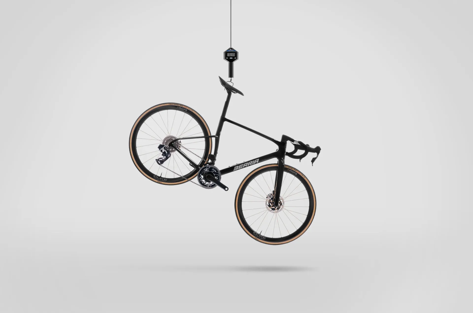 Bicicleta negra suspendida de una lámpara de techo sobre un fondo blanco.