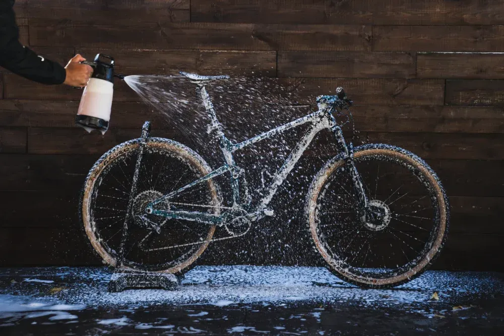 Una persona rociando agua jabonosa sobre una bicicleta de montaña. Fondo de madera marrón.