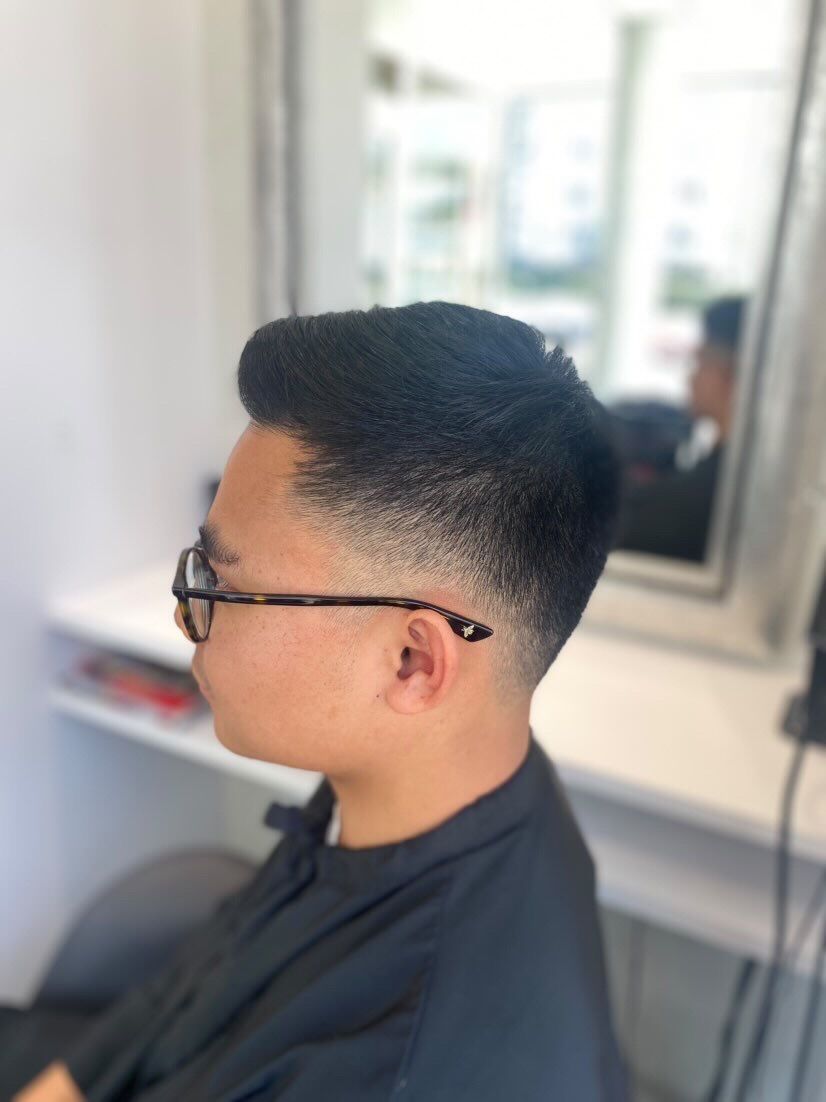 Homme portant des lunettes, cheveux courts et une mèche décolorée sur le côté. À l'intérieur, près d'un miroir.