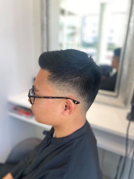 Homme portant des lunettes, cheveux courts et une mèche décolorée sur le côté. À l'intérieur, près d'un miroir.
