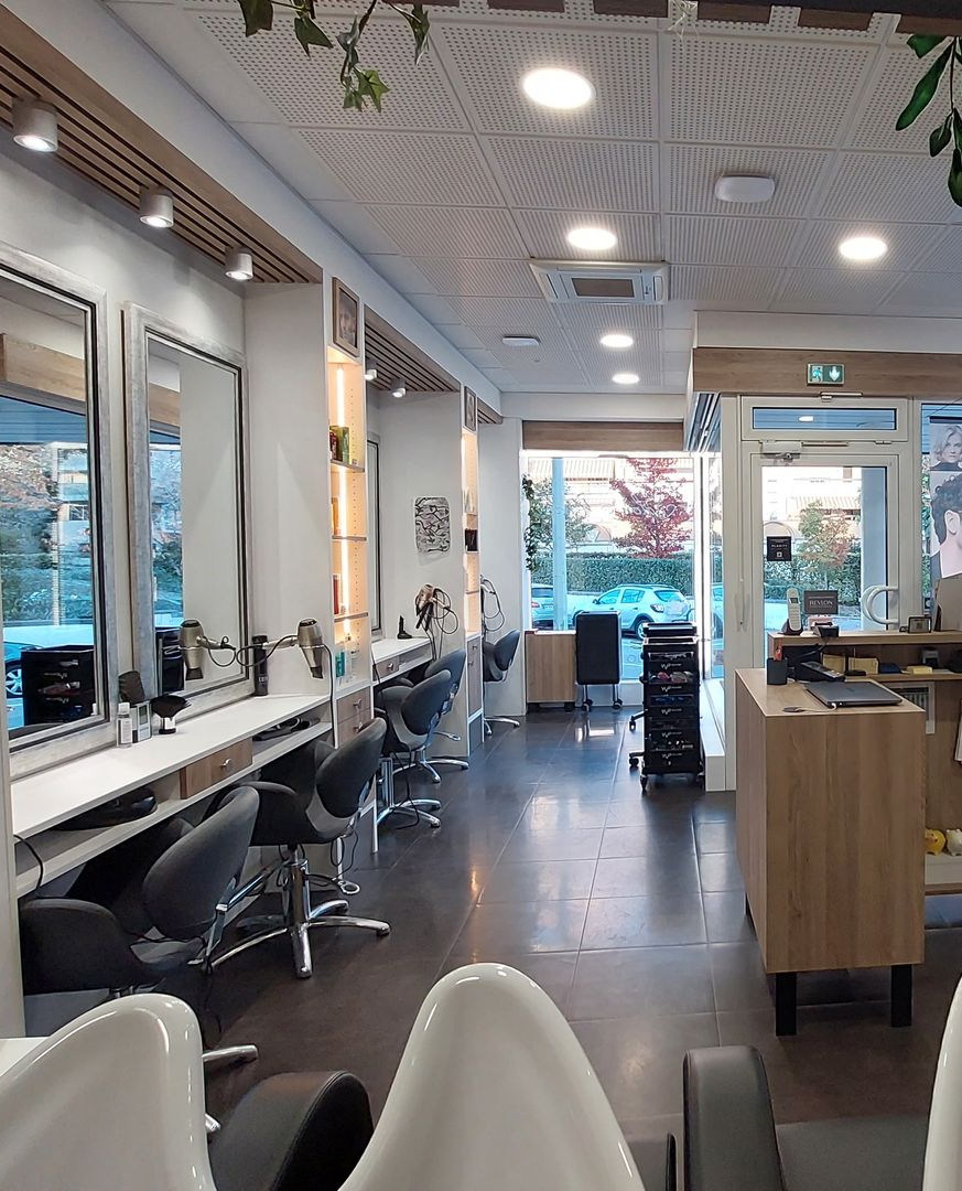 Intérieur d'un salon de coiffure avec miroirs, chaises et postes de coiffage ; lumière naturelle dès l'entrée.