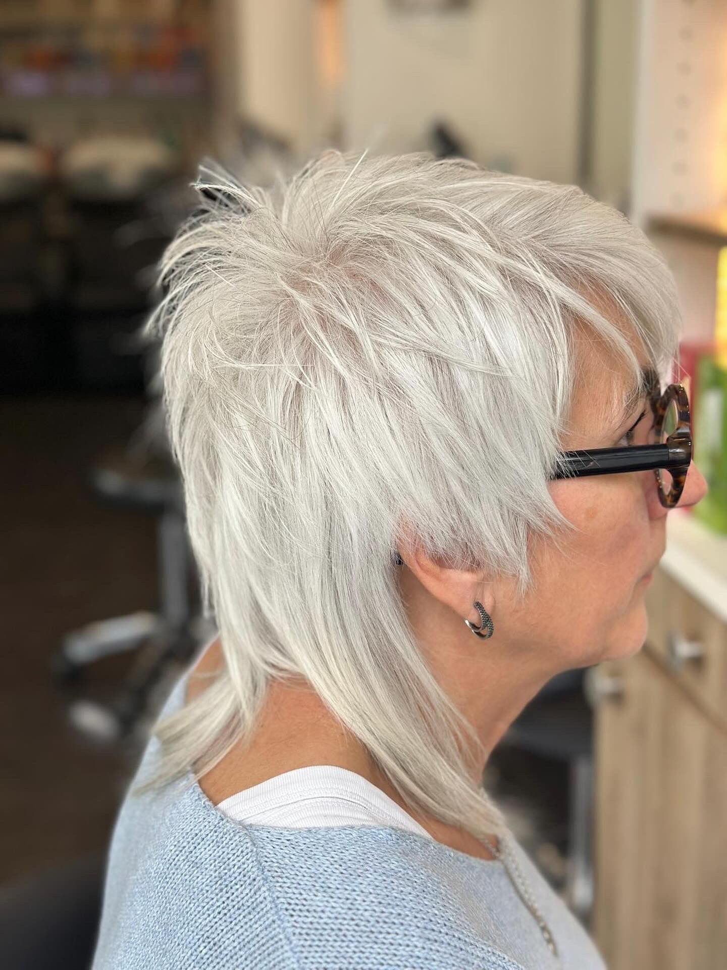 Femme aux cheveux courts, texturés et argentés, portant des lunettes, dans un salon de coiffure.