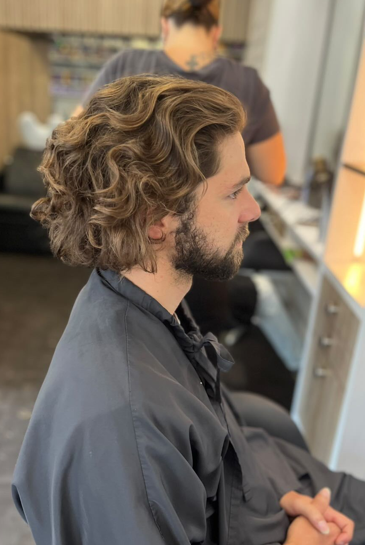 Un homme aux cheveux bruns bouclés se fait couper les cheveux, dans un salon de coiffure.