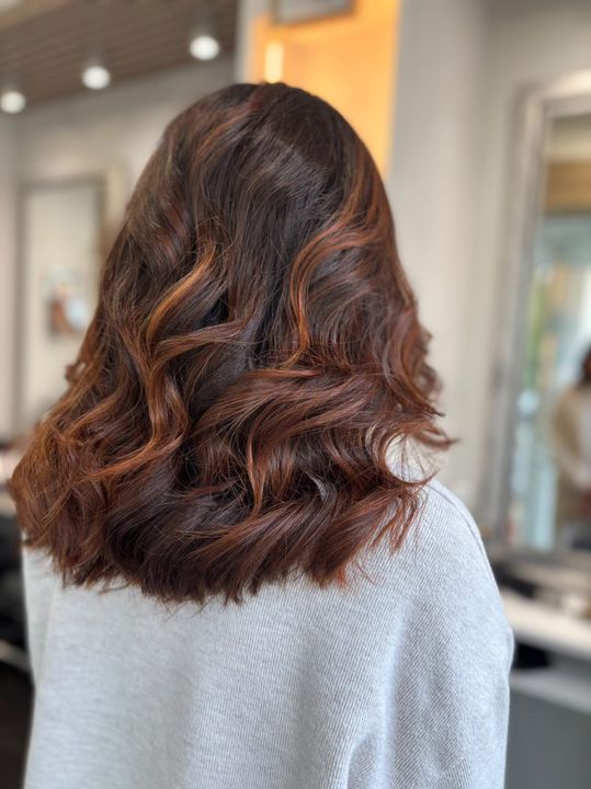Cheveux ondulés brun foncé avec des reflets cuivrés, coiffés en salon.