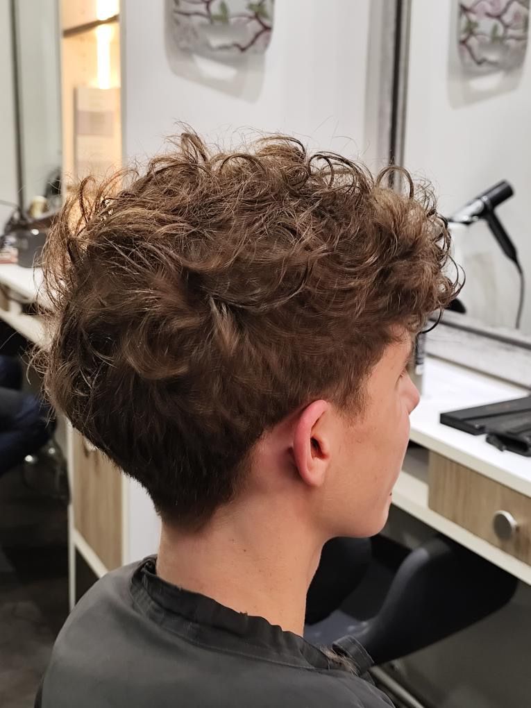 Personne aux cheveux bruns et bouclés ; coupe courte sur les côtés et à l'arrière, réalisée en salon de coiffure.