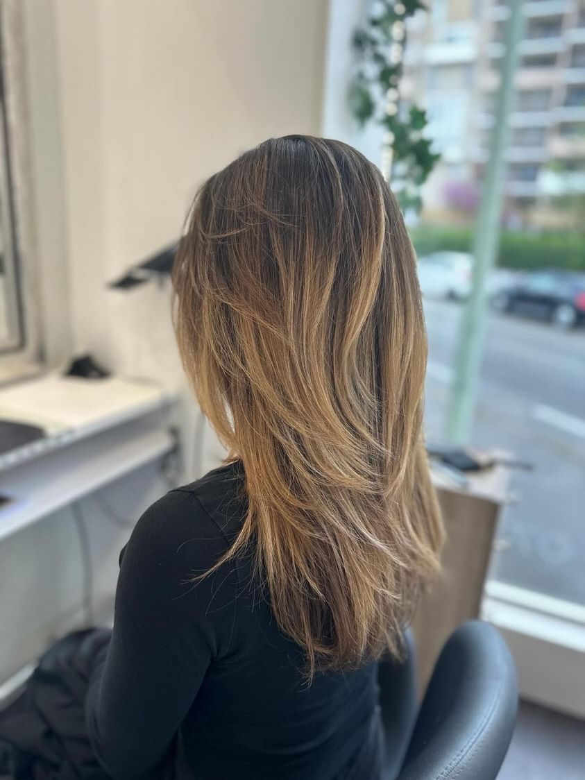 Femme aux cheveux ondulés et dégradés, assise dans un salon de coiffure, regardant ailleurs que vers la caméra.